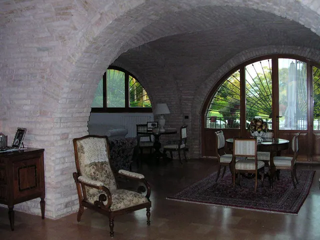 Una sala a volte con poltrona antica e tavolo rotondo davanti alle porte ad arco che danno sul giardino